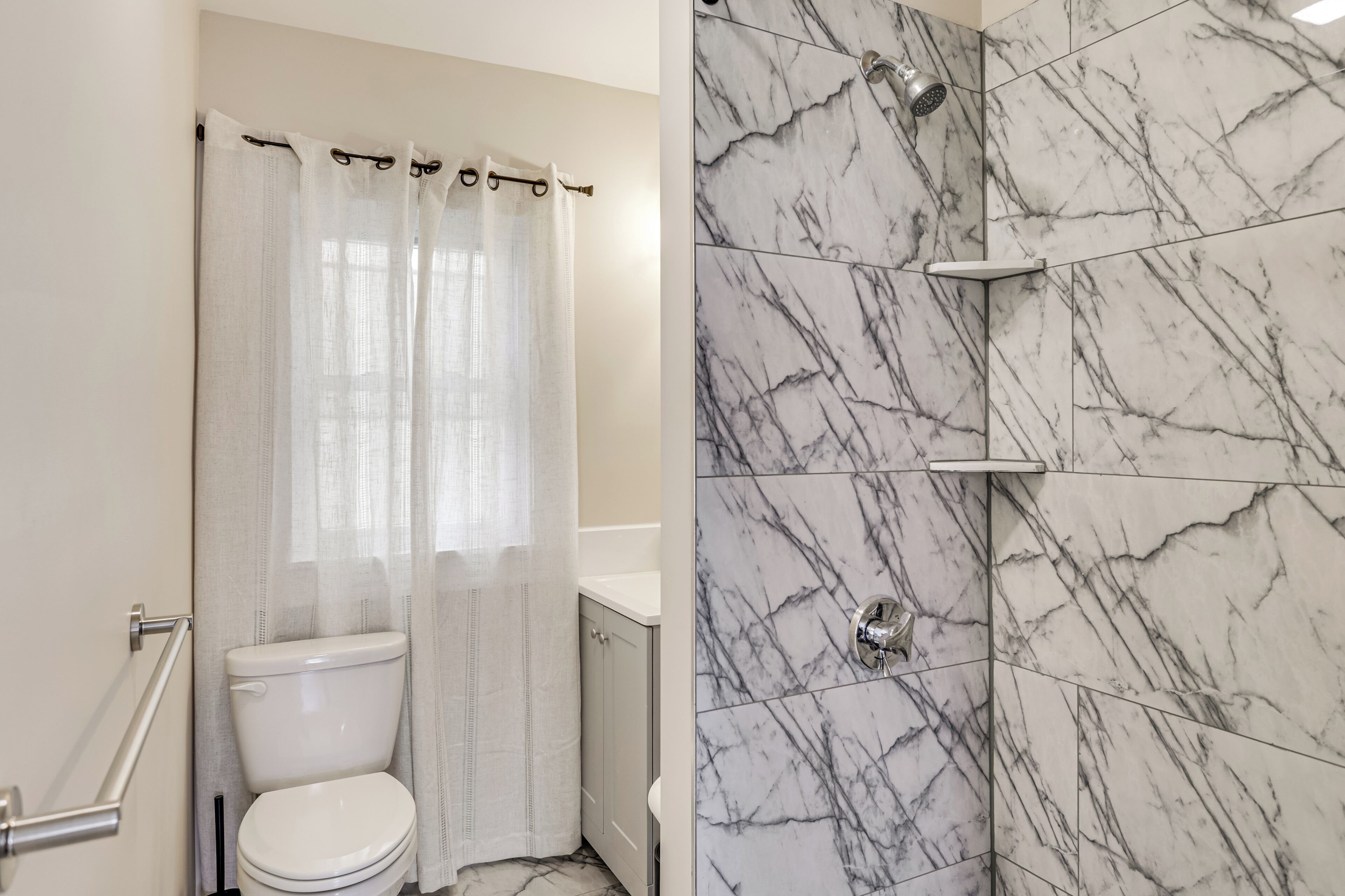 Une salle de bain comprenant des toilettes, une douche aux parois carrelées de marbre et une porte de douche en verre.