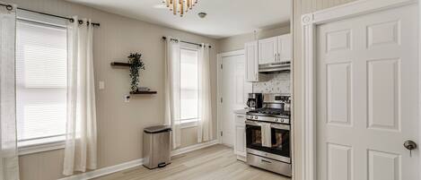 A modern kitchen with white cabinetry, a stainless steel stove, and a chandelier.