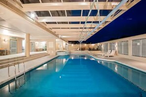 Ein Innenpool mit klarem Wasser, umgeben von Liegestühlen und einem überdachten Bereich mit Dachkonstruktion.