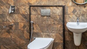 Een badkamer met een marmeren wand, toilet, wastafel en spiegel.