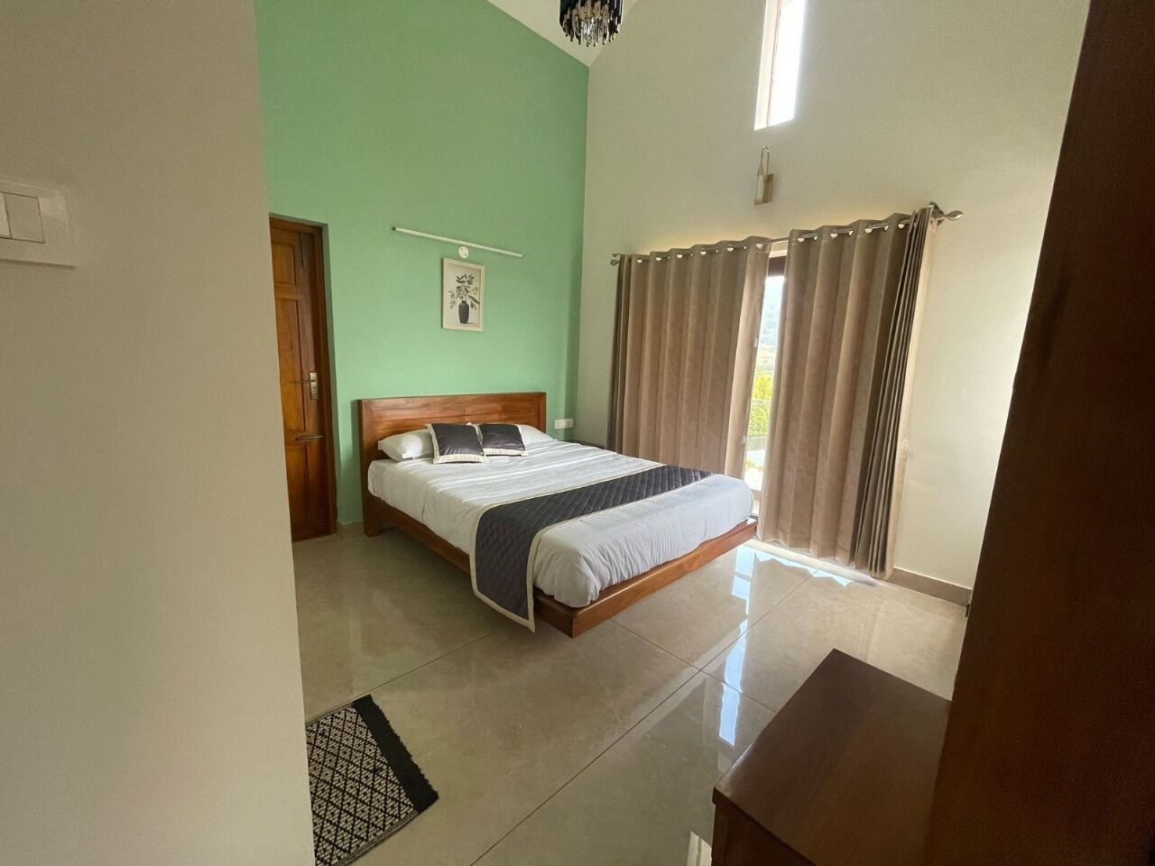A bedroom with a bed, a door, a window with curtains, and a light fixture.