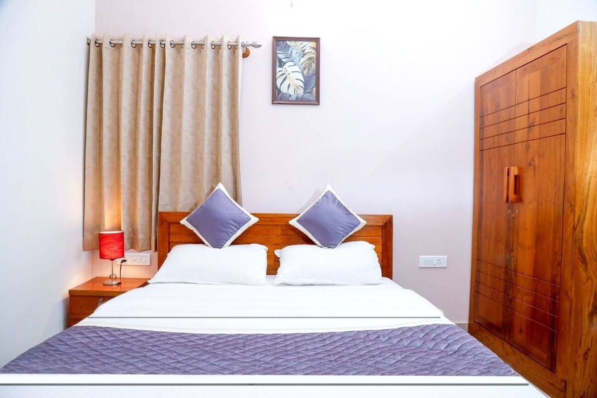 A neatly made bed with a wooden headboard, a bedside table with a lamp, a wardrobe, and a framed picture on the wall.