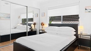 A modern bedroom with a large bed, a bedside table with a lamp, a mirror, and a window with blinds. - Spacious 3-Bed House in Leafy Paddington (Paddington)
