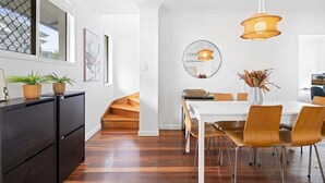A modern dining area with a white table, wooden chairs, and a hanging light fixture. - Spacious 3-Bed House in Leafy Paddington (Paddington)