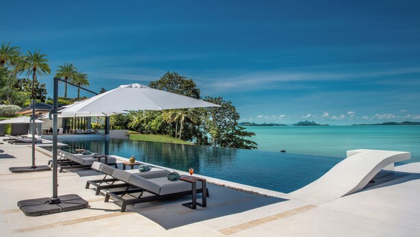 Un espace aménagé au bord de la piscine, avec des chaises longues, une table et des parasols.