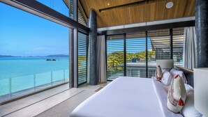 Une chambre d’hôtel moderne dotée d’un grand lit, offrant une vue sur la mer et disposant d’un balcon avec une balustrade en verre.