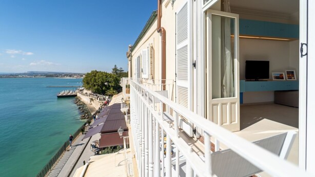 Un balcon avec vue sur la mer, un coin repas avec des sièges extérieurs et un intérieur moderne équipé d’un téléviseur.