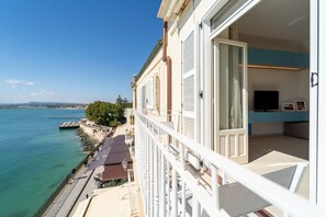 A balcony with a view of the sea, a dining area with outdoor seating, and a modern interior with a TV. - Alfeo Seafront - Sunset view (Siracusa)