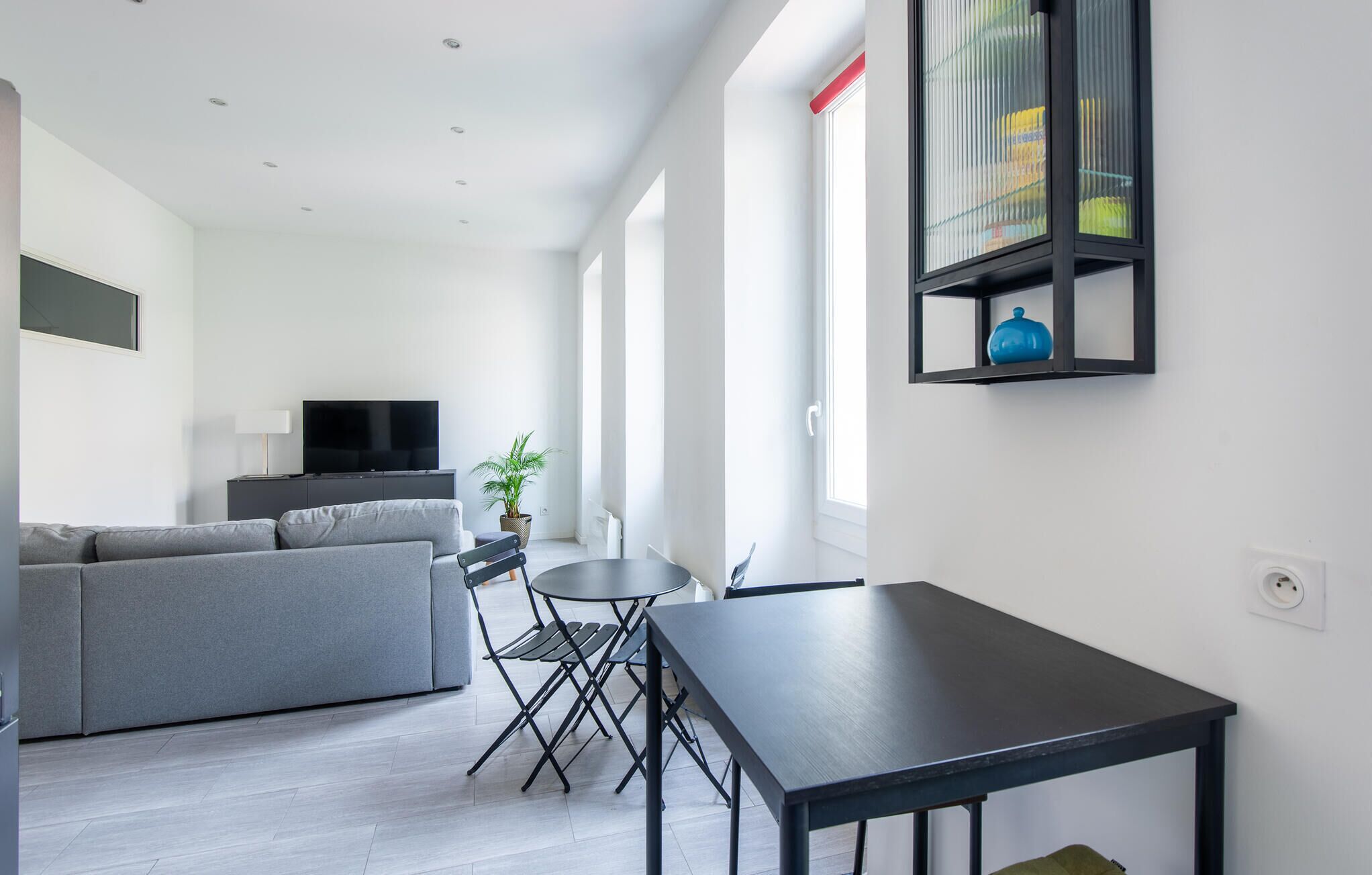 A modern living room with a grey sofa, a black dining table, and a small round table with chairs.