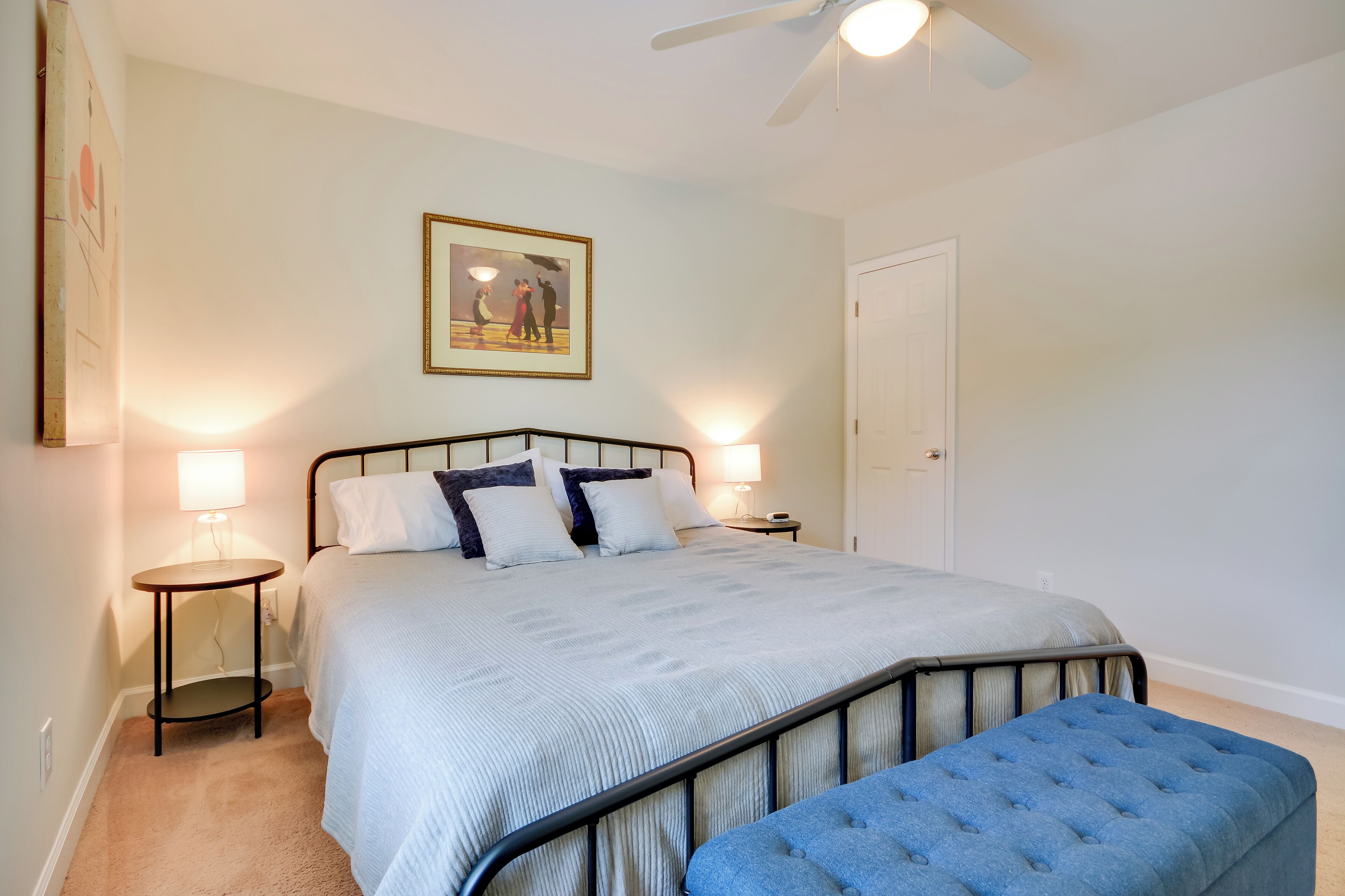 A bedroom with a bed, bedside lamps, a ceiling fan, and a framed picture on the wall.