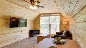 A cozy cabin interior with a wooden interior, a fireplace, a dining table, and a ceiling fan.