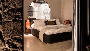 Un dormitorio moderno con una cama grande, una pared de piedra y vistas a un baño por una ventana.