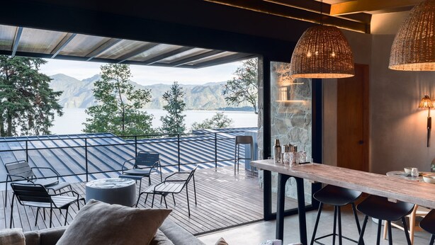 Un espacio de comedor exterior moderno con una terraza de madera, sillas de metal y un taburete de bar.