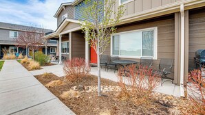 A modern two-story building with a covered patio area, outdoor seating, and a landscaped garden.