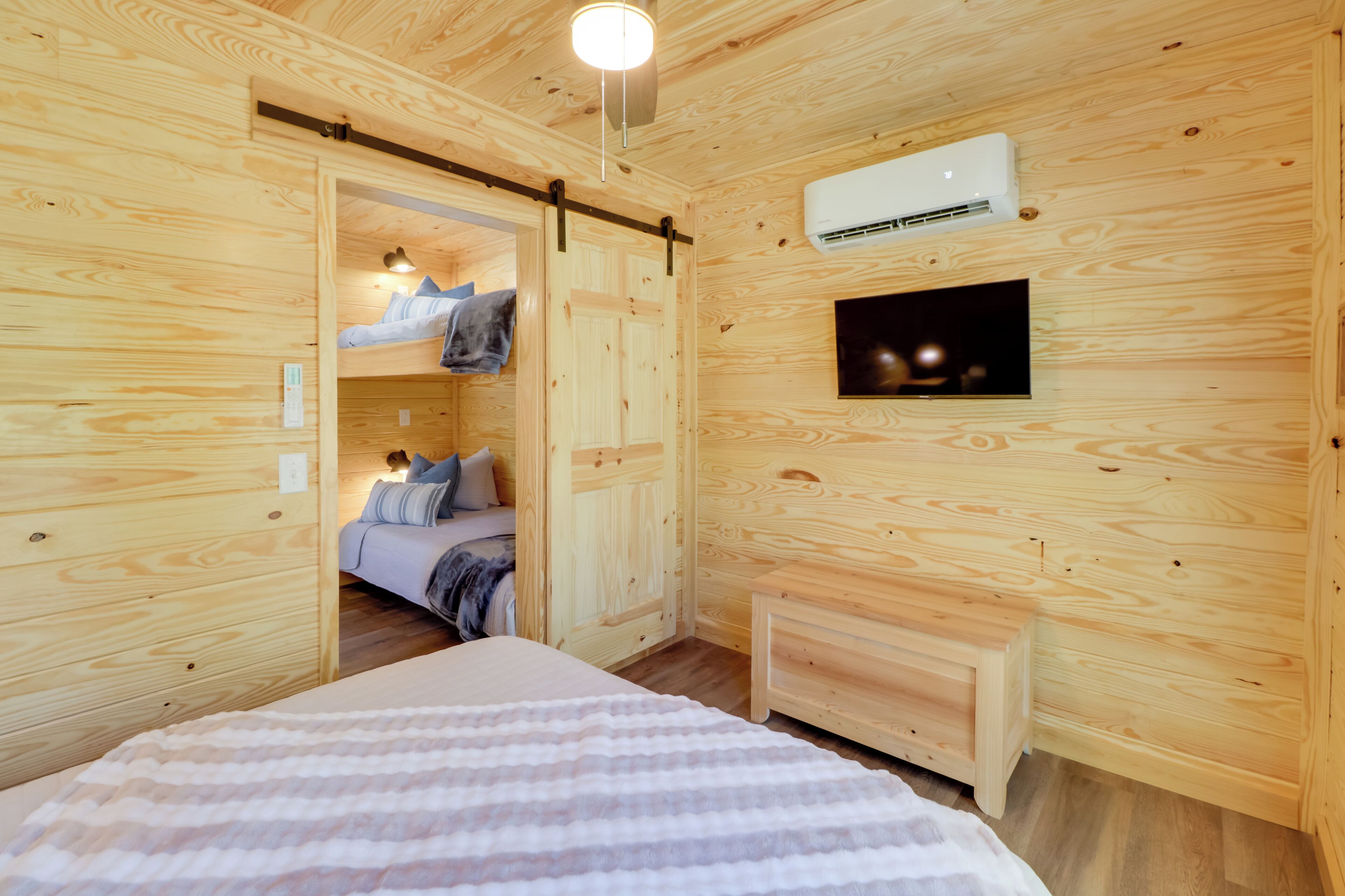 Una habitación de cabaña de madera con cama, un banco, un televisor y un aire acondicionado.