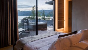 A bedroom with a large bed, a view of a hot tub and mountains through a sliding glass door.