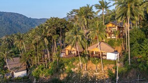 A tropical resort with multiple wooden cabins surrounded by lush palm trees and a mountain backdrop. - RoomQuest THEVA Resort koh Samui  (Koh Samui)