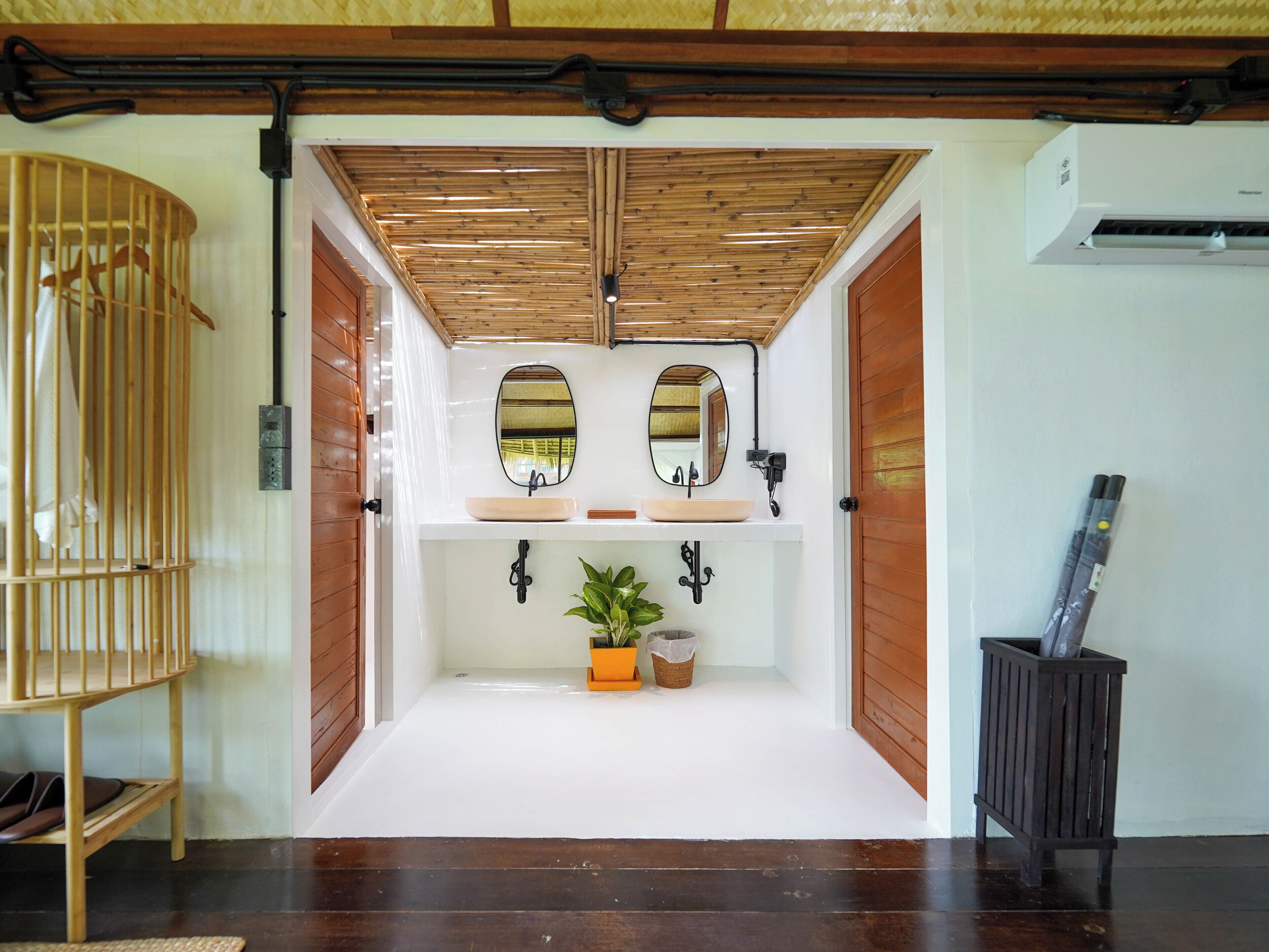 A bathroom with two sinks, mirrors, a potted plant, and a wooden bench.