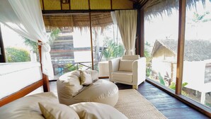 A bedroom with a bed, a sofa, and a chair, large windows with curtains, and a view of the outside. - RoomQuest THEVA Resort koh Samui  (Koh Samui)