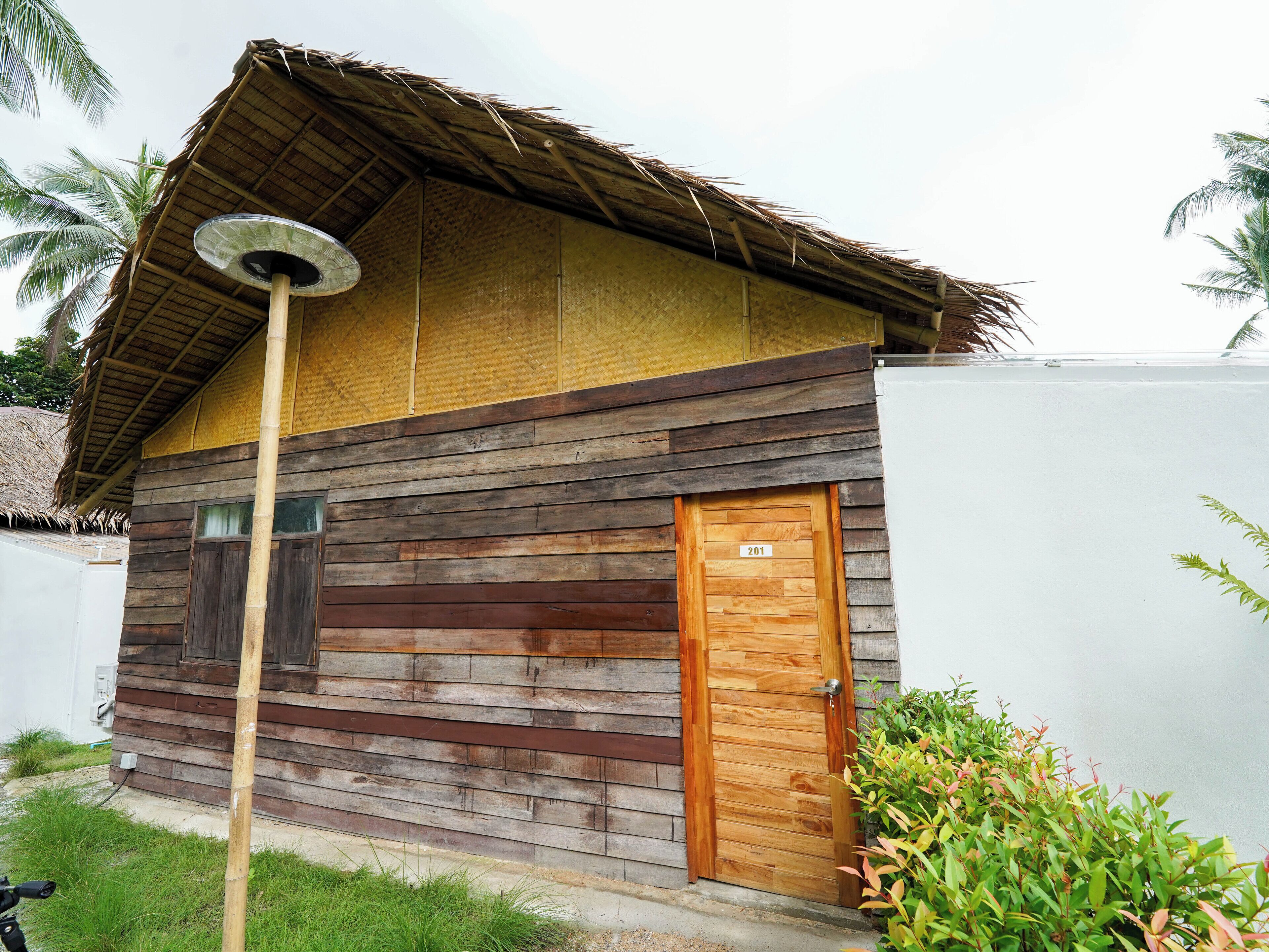 Una casa de madera con techo de paja, una puerta de madera con la etiqueta '201' y un pequeño porche.