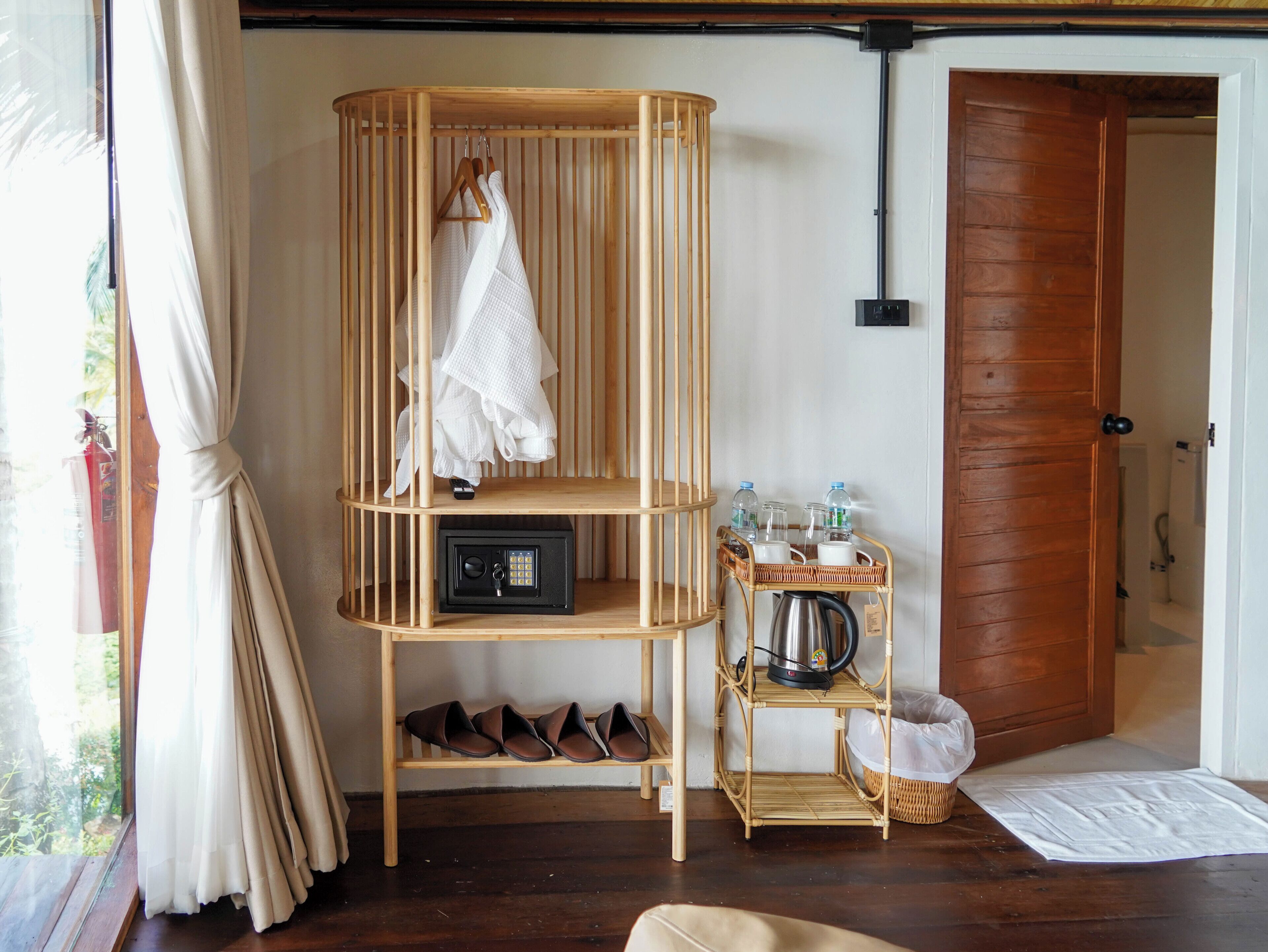 A room with a wooden shoe rack, a small table with bottles and a kettle, and a door.