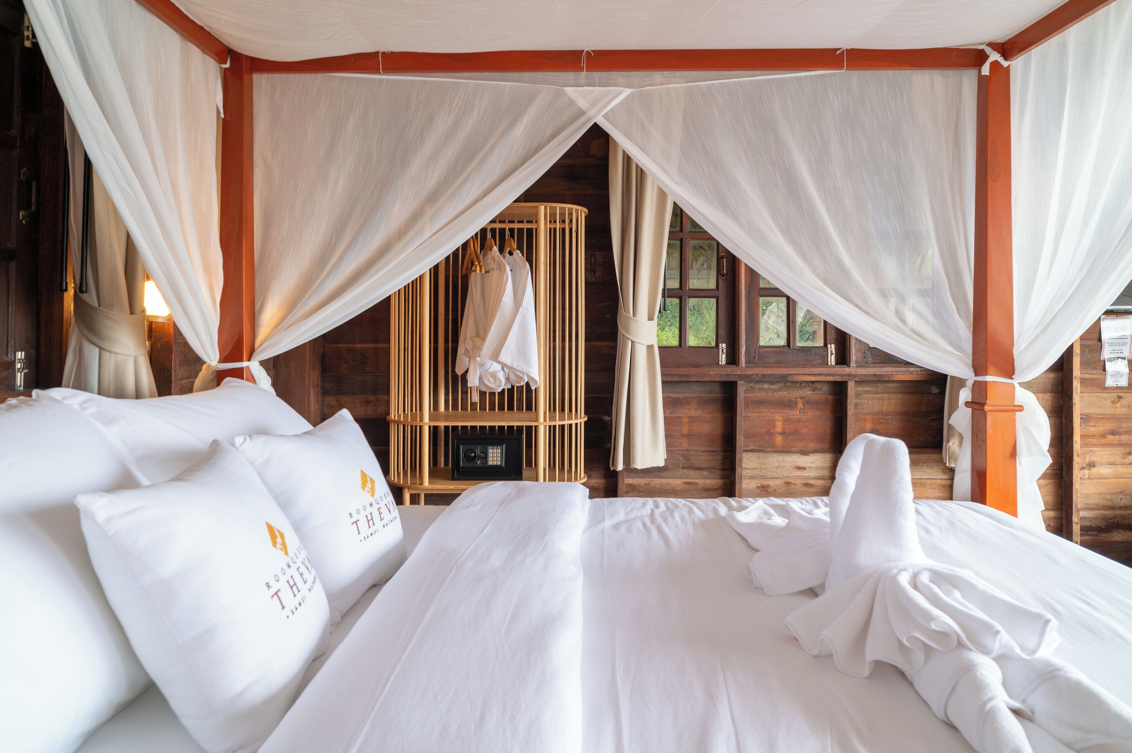 A room with a canopy bed, wooden furniture, and a wardrobe with hanging clothes.