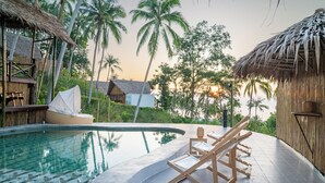 A poolside area with lounge chairs, a thatched-roof structure, and a view of palm trees. - RoomQuest THEVA Resort koh Samui  (Koh Samui)