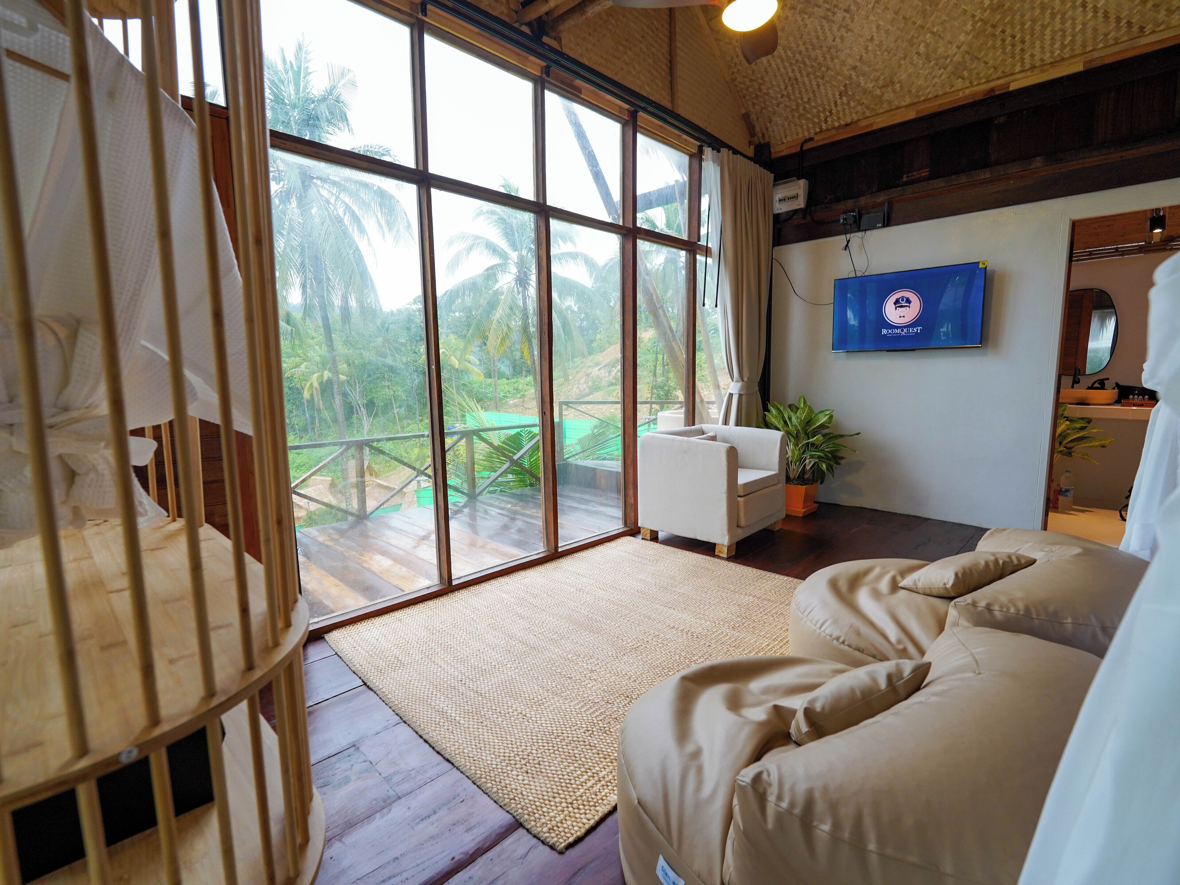 A spacious room with a large sliding glass door leading to a balcony, a comfortable sofa, a small table, and a potted plant.