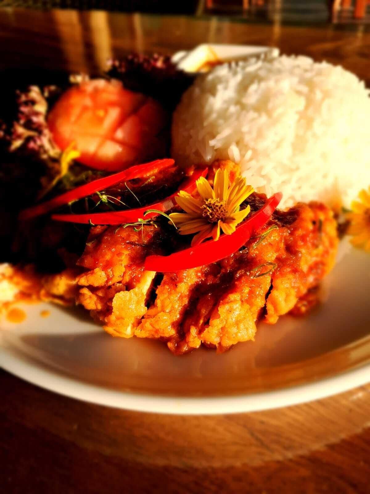 Une assiette contenant un plat principal, un accompagnement de riz et une garniture composée de fines tranches de piment rouge et d’une fleur.