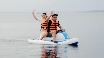 Two people on a watercraft with life jackets, floating on calm water.