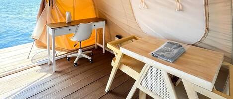 A tent with a wooden desk and chair, a small table, and a view of the sea.