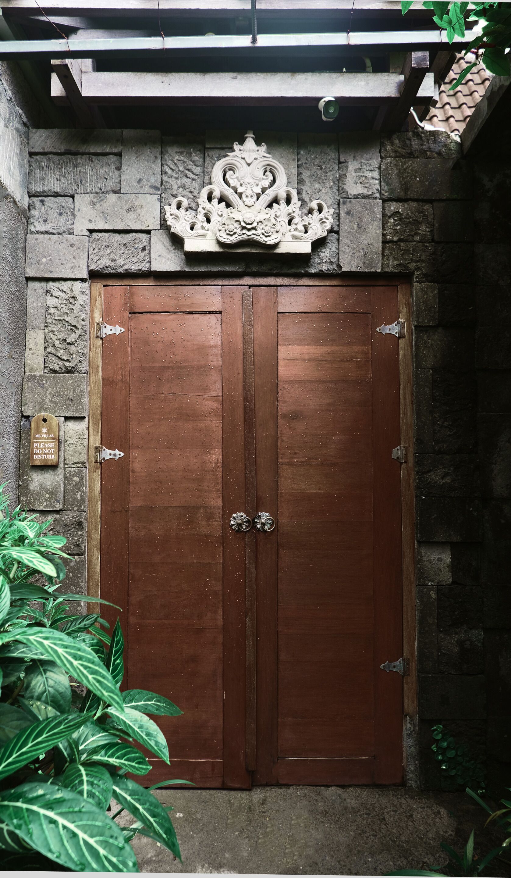 A wooden double door with a stone wall and a metal plaque above it.