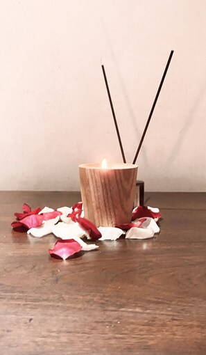 A candle in a wooden holder with two incense sticks, surrounded by scattered rose petals on a wooden surface. - ME Villas Echo Beach (Canggu)