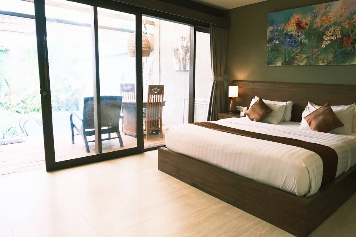 A hotel room with a large bed, a painting on the wall, and a view through the glass door.