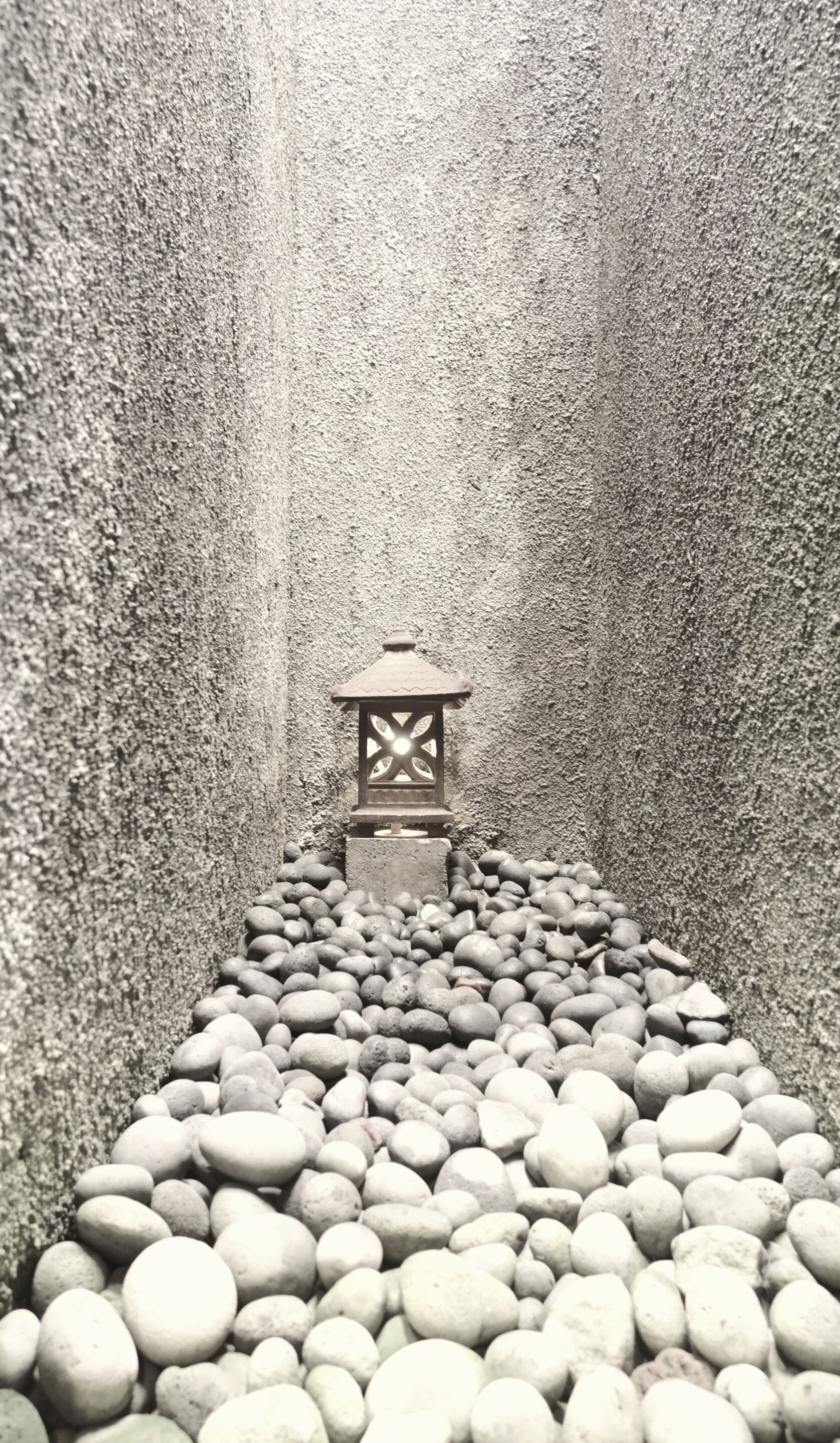 Ein schmaler Pfad, gesäumt von glatten Kieselsteinen, der zu einem laternenartigen Bauwerk führt.