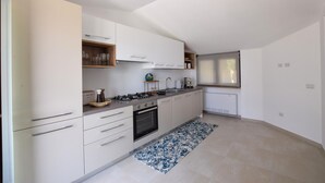 Uma cozinha moderna com armários brancos, fogão a gás, forno, pia e uma janela com persiana.