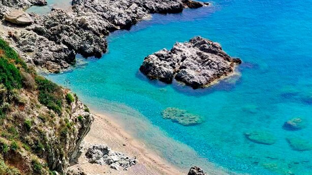 Paisagem costeira com formações rochosas e águas azul-claras.