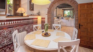 Un coin repas avec une table ronde, des chaises blanches et un set de table en fibres tressées.