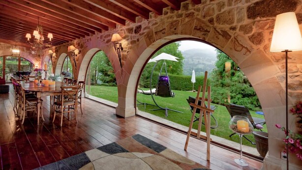 Un vaste espace dédié à la salle à manger, avec une table et des chaises en bois, des arches en pierre et une vue sur le jardin.