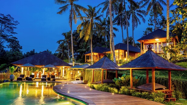 Ein Resort mit Schwimmbad, Holzterrasse und strohgedeckten Gebäuden.