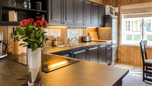 A modern kitchen with dark cabinets, a stainless steel island, and a view of the outside through a window.