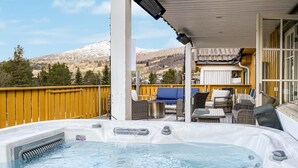 A hot tub with a view of mountains, outdoor furniture, and a yellow fence.
