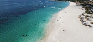 A beach with clear turquoise water, white sand, and a few umbrellas.