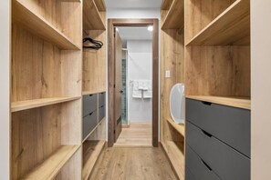 A narrow hallway with wooden shelving on both sides and a door at the end leading to a bathroom with a tiled wall and a towel rack.