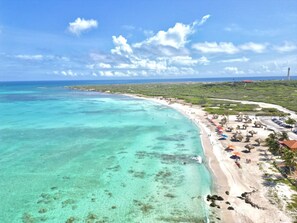 Ein Küstenstrand mit klarem türkisblauem Wasser, einem sandigen Ufer und einer Reihe von strohgedeckten Gebäuden direkt am Strand.