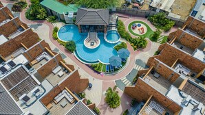 An aerial view of a resort with a central pool, multiple lounge areas, and a variety of outdoor spaces.