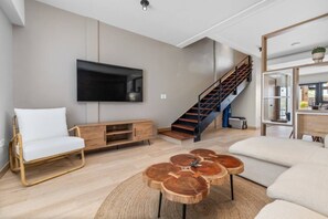 A modern living room with a flat-screen TV, a staircase, and a dining area.