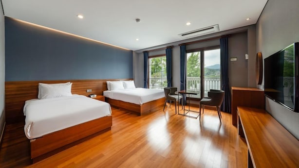 Habitació d'hotel amb dos llits, televisió, balcó amb vistes i taula petita amb cadires.