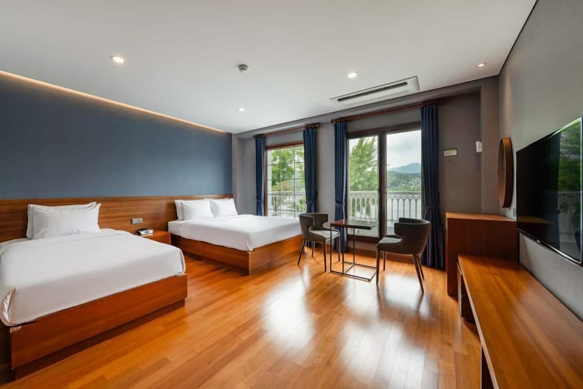 A hotel room with two beds, a TV, a balcony with a view, and a small table with chairs.
