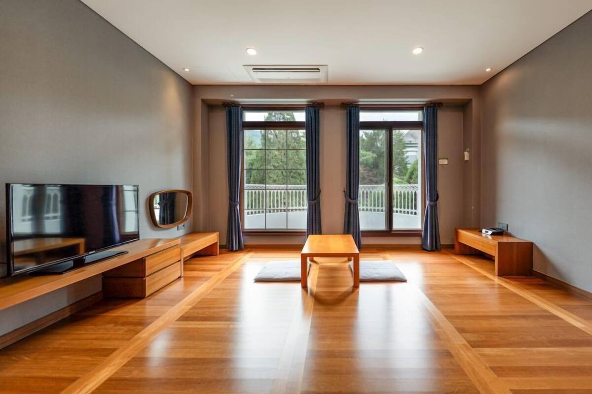 A spacious room with a wooden floor, a flat-screen TV, a mirror, and a bench.